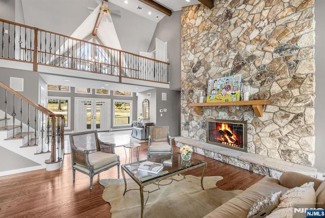 living room featuring french doors, a stone fireplace, beam ceiling, and wood finished floors