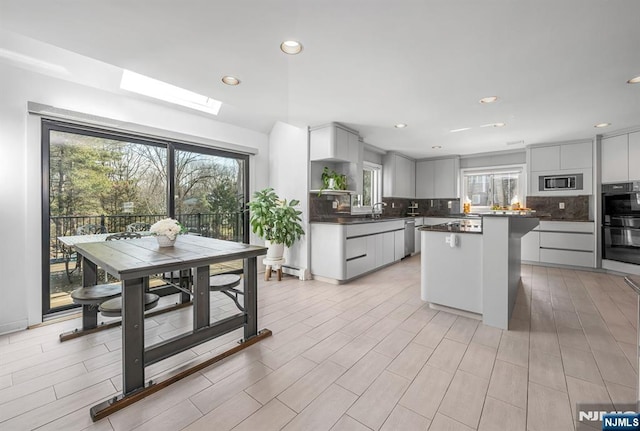 kitchen with a sink, a kitchen island, appliances with stainless steel finishes, decorative backsplash, and dark countertops