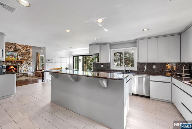 kitchen featuring tasteful backsplash, visible vents, dishwasher, a breakfast bar, and a stone fireplace