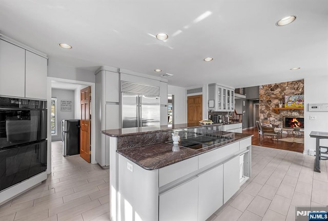 kitchen featuring glass insert cabinets, white cabinetry, a fireplace, and black appliances