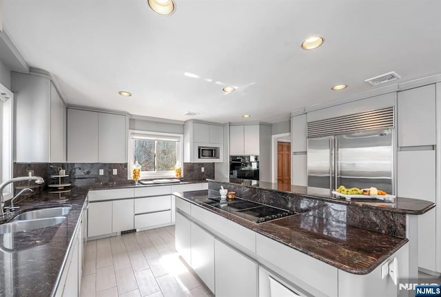 kitchen with dark stone countertops, a center island, built in appliances, white cabinetry, and a sink