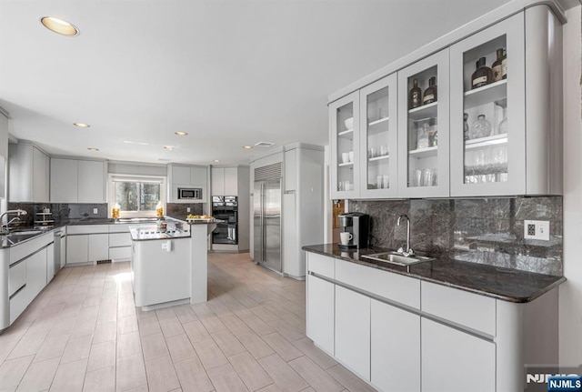 kitchen with modern cabinets, appliances with stainless steel finishes, glass insert cabinets, a center island, and a sink