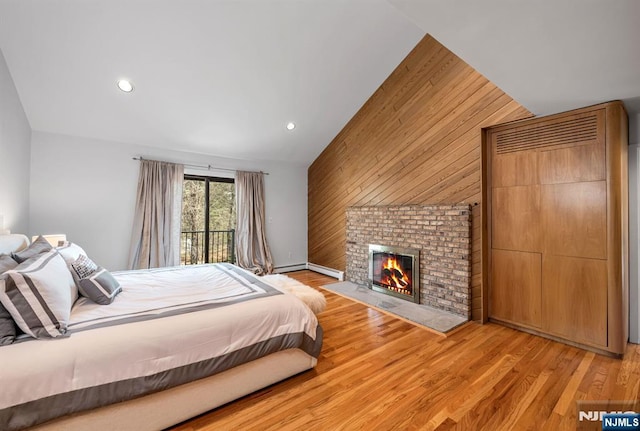 bedroom featuring light wood finished floors, wooden walls, lofted ceiling, a brick fireplace, and recessed lighting