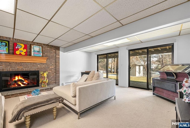 living area featuring a brick fireplace, light colored carpet, and a drop ceiling