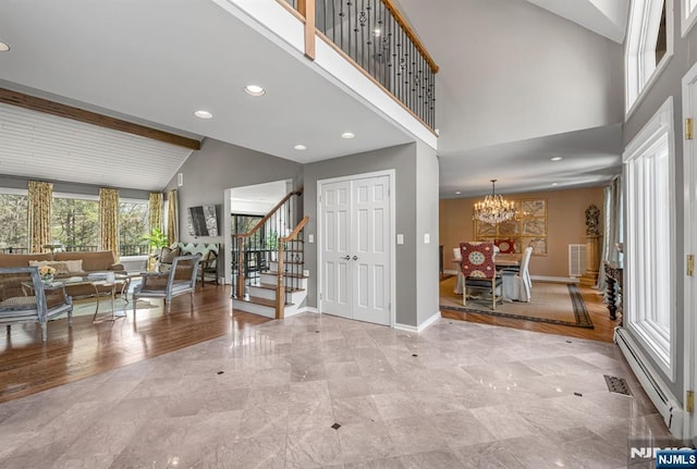 foyer entrance with stairway, baseboards, a baseboard heating unit, and high vaulted ceiling