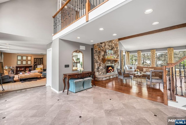 living area with visible vents, stairway, a towering ceiling, a stone fireplace, and baseboards