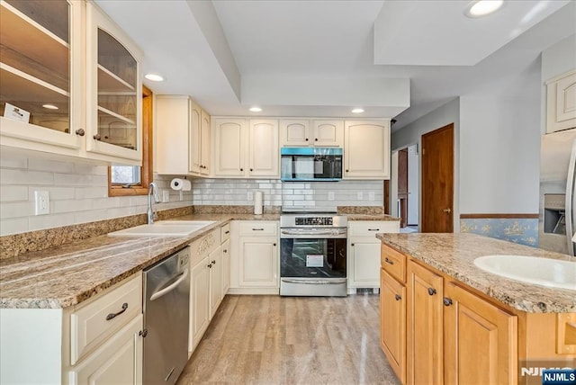 kitchen featuring stainless steel appliances, light wood-style floors, glass insert cabinets, a sink, and light stone countertops