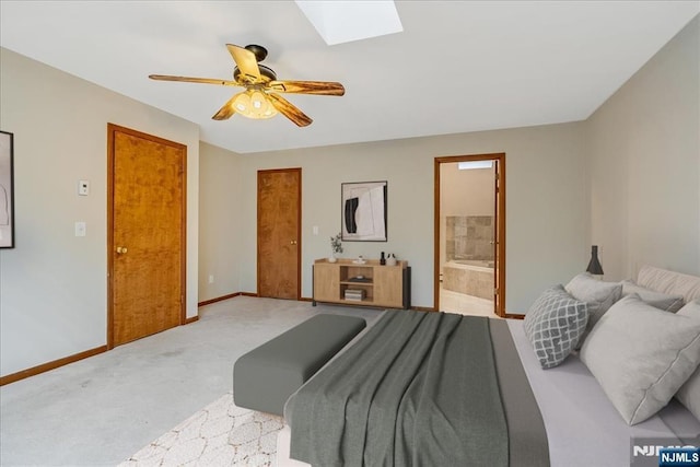 bedroom featuring connected bathroom, light colored carpet, a skylight, a ceiling fan, and baseboards