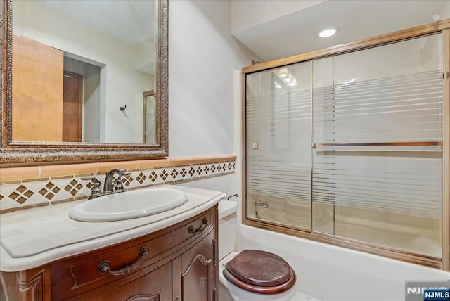 bathroom with toilet, shower / bath combination with glass door, backsplash, and vanity