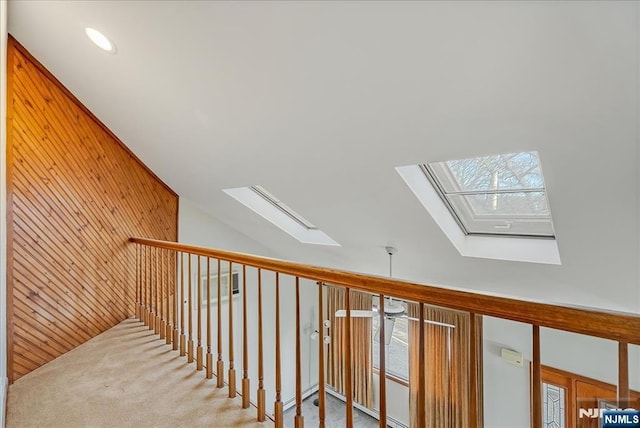 hallway with lofted ceiling with skylight, recessed lighting, carpet flooring, and wooden walls