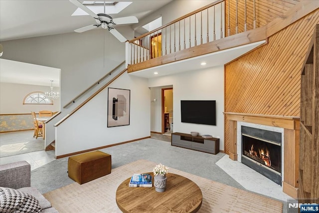 living area featuring stairs, high vaulted ceiling, a fireplace with flush hearth, and ceiling fan with notable chandelier