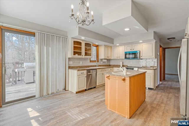 kitchen featuring a center island with sink, glass insert cabinets, freestanding refrigerator, decorative light fixtures, and light stone countertops