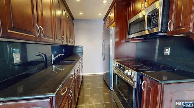 kitchen with dark tile patterned flooring, appliances with stainless steel finishes, dark stone countertops, a sink, and backsplash