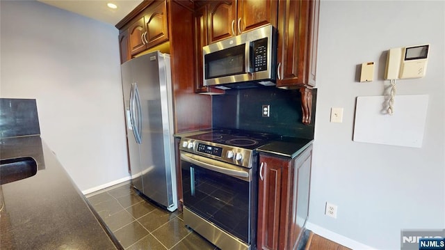 kitchen featuring dark tile patterned floors, baseboards, appliances with stainless steel finishes, decorative backsplash, and dark countertops