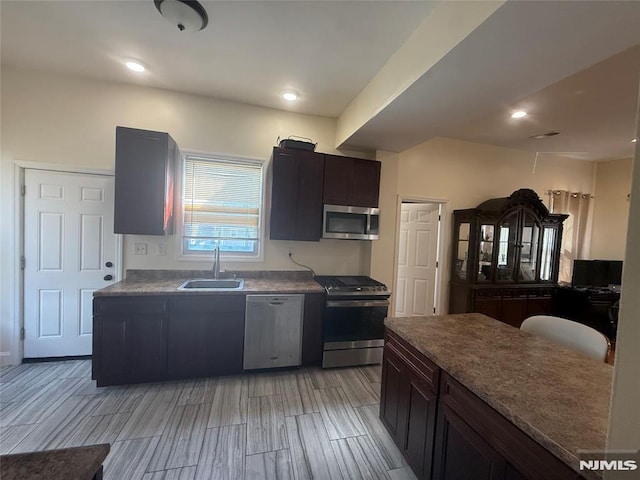 kitchen with stainless steel appliances, dark brown cabinets, a sink, and wood tiled floor