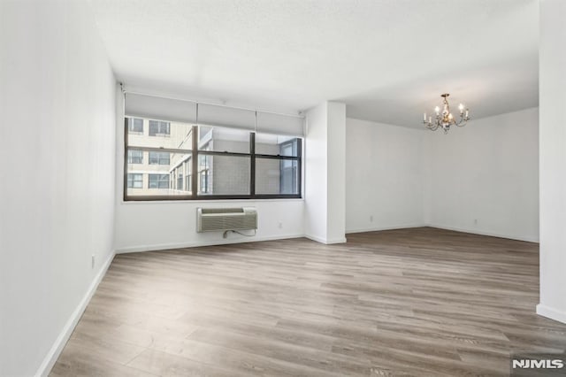 empty room featuring baseboards, a wall mounted air conditioner, wood finished floors, and an inviting chandelier