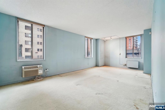 unfurnished room with radiator, a wall mounted air conditioner, a textured ceiling, carpet floors, and track lighting