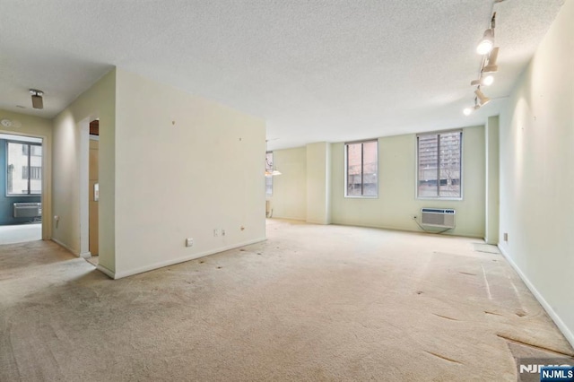 unfurnished living room featuring carpet, a wall mounted air conditioner, a textured ceiling, and track lighting