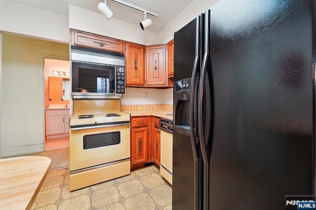 kitchen featuring a textured ceiling, light countertops, brown cabinetry, black refrigerator with ice dispenser, and white range with electric cooktop