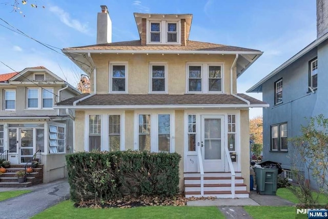 american foursquare style home with entry steps, roof with shingles, a chimney, and stucco siding