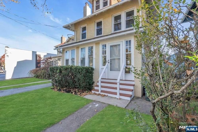 american foursquare style home featuring entry steps, stucco siding, a chimney, and a front yard