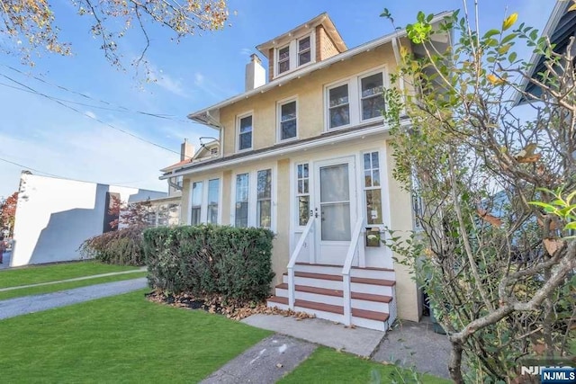 traditional style home with entry steps, stucco siding, a chimney, and a front yard