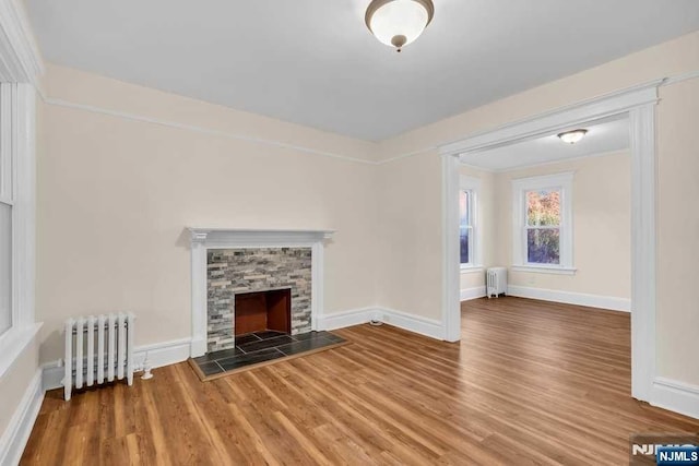 unfurnished living room with radiator, a fireplace, baseboards, and wood finished floors