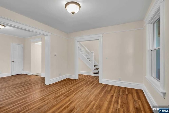 empty room with stairs, baseboards, and wood finished floors