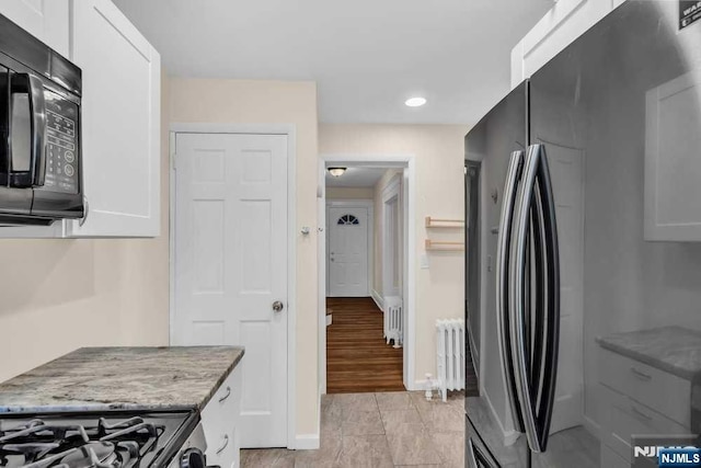 kitchen with black appliances, light stone counters, radiator heating unit, and white cabinets