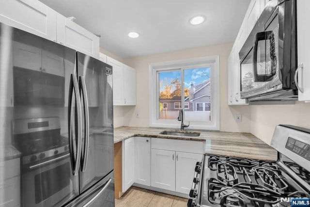 kitchen featuring black microwave, light stone counters, white cabinetry, and stainless steel gas stove