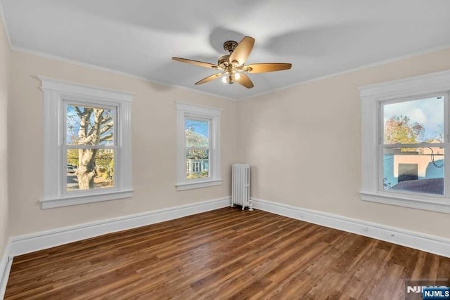 empty room featuring ornamental molding, radiator, baseboards, and wood finished floors