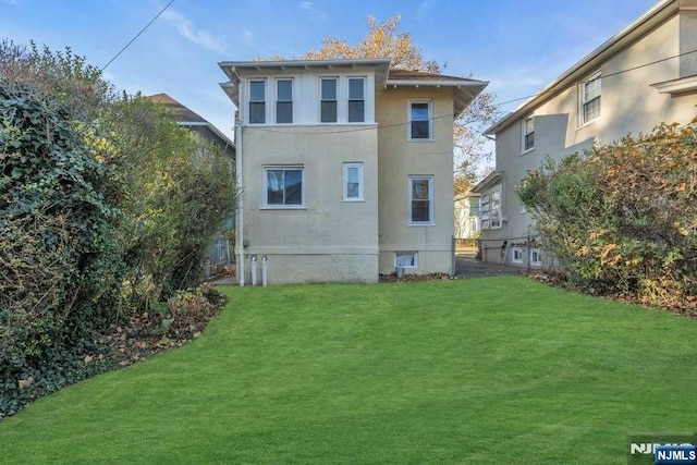 rear view of house featuring a lawn and stucco siding