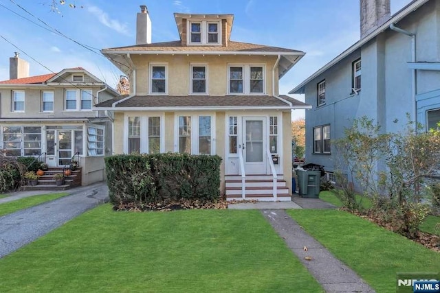 american foursquare style home featuring entry steps, a chimney, a front lawn, and stucco siding