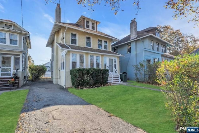 american foursquare style home featuring driveway, a chimney, a front yard, and stucco siding