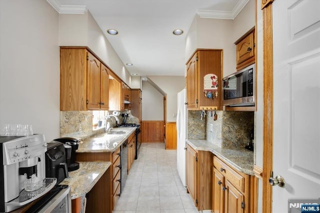 kitchen featuring light stone counters, a sink, appliances with stainless steel finishes, wainscoting, and brown cabinets