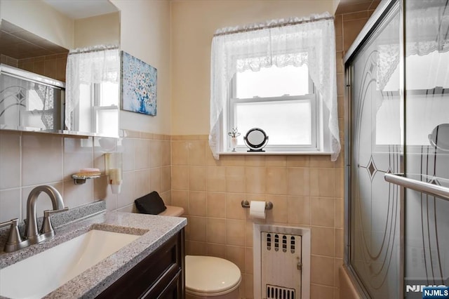 bathroom featuring shower / bath combination with glass door, tile walls, radiator, toilet, and vanity