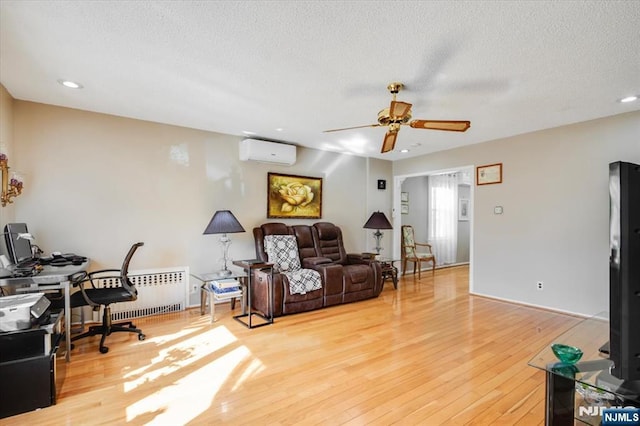 living room featuring a wall unit AC, radiator, a ceiling fan, a textured ceiling, and light wood-type flooring