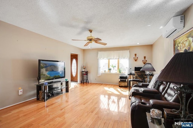 living room with a textured ceiling, a ceiling fan, baseboards, light wood finished floors, and a wall mounted air conditioner