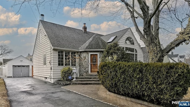 view of front facade with aphalt driveway, a detached garage, a chimney, a shingled roof, and an outdoor structure