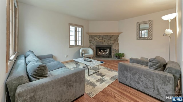 living room featuring a fireplace, wood finished floors, visible vents, and baseboards