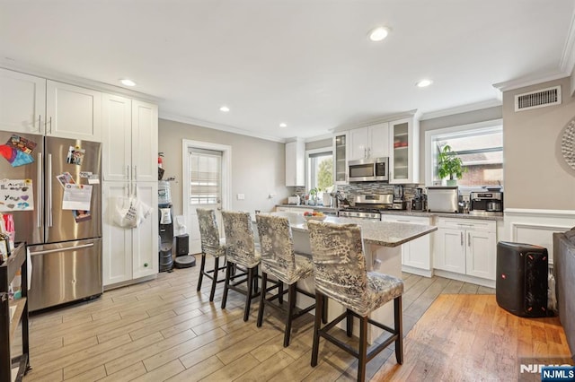 kitchen with stainless steel appliances, light wood-style flooring, visible vents, and crown molding