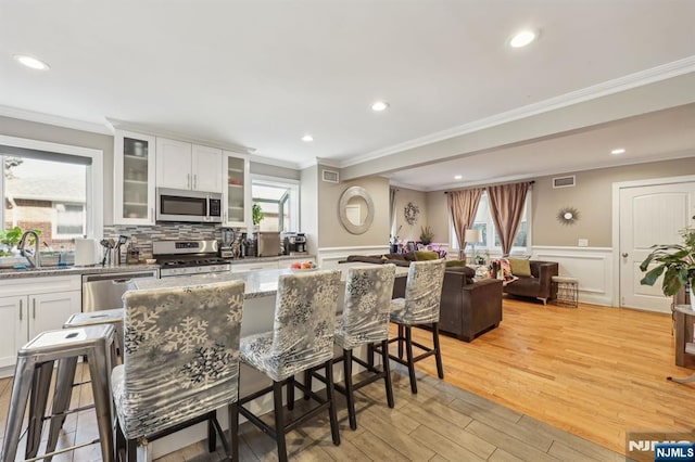 kitchen with stainless steel appliances, white cabinets, wainscoting, light wood-type flooring, and a kitchen bar