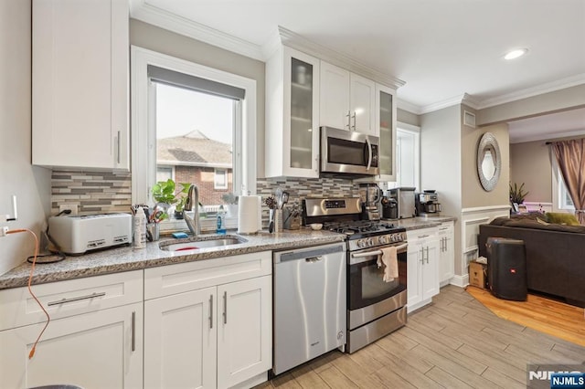 kitchen featuring crown molding, appliances with stainless steel finishes, white cabinets, a sink, and light wood-type flooring