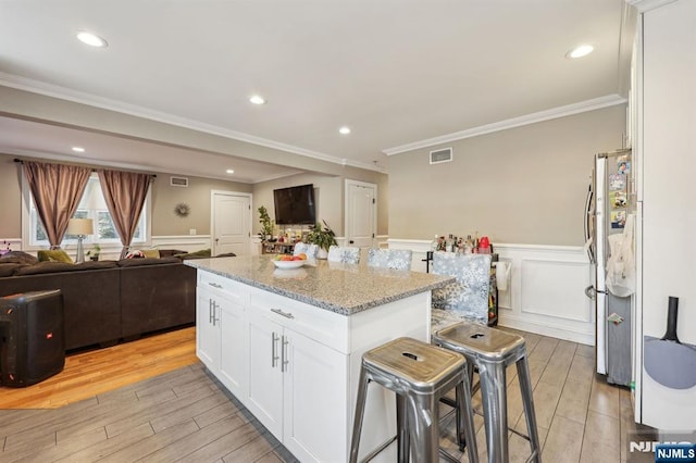 kitchen with visible vents, white cabinets, a wainscoted wall, a center island, and wood tiled floor