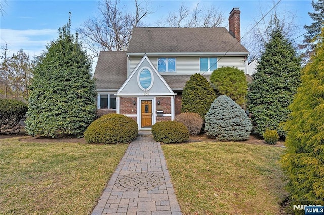 view of front of property with brick siding, a chimney, a front lawn, and roof with shingles