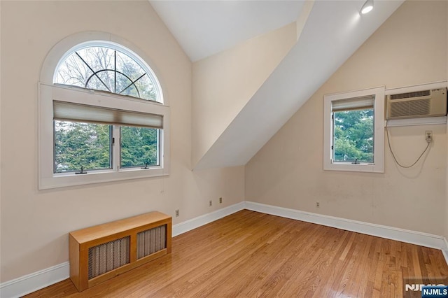 additional living space featuring baseboards, visible vents, a wall unit AC, wood finished floors, and vaulted ceiling