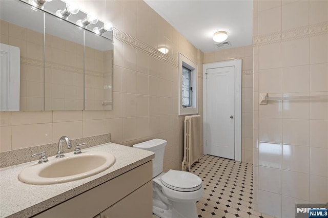 bathroom with toilet, visible vents, vanity, tile walls, and radiator heating unit