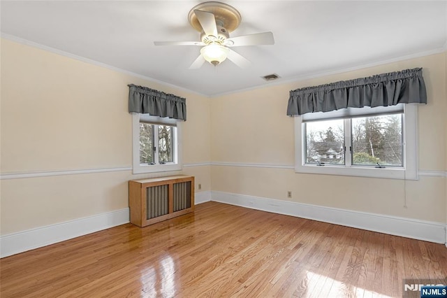 empty room with radiator heating unit, crown molding, baseboards, and wood finished floors