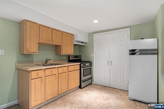 kitchen with light countertops, a sink, under cabinet range hood, stainless steel gas range oven, and fridge