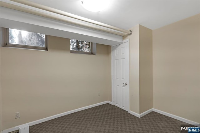 below grade area with dark colored carpet, visible vents, and baseboards